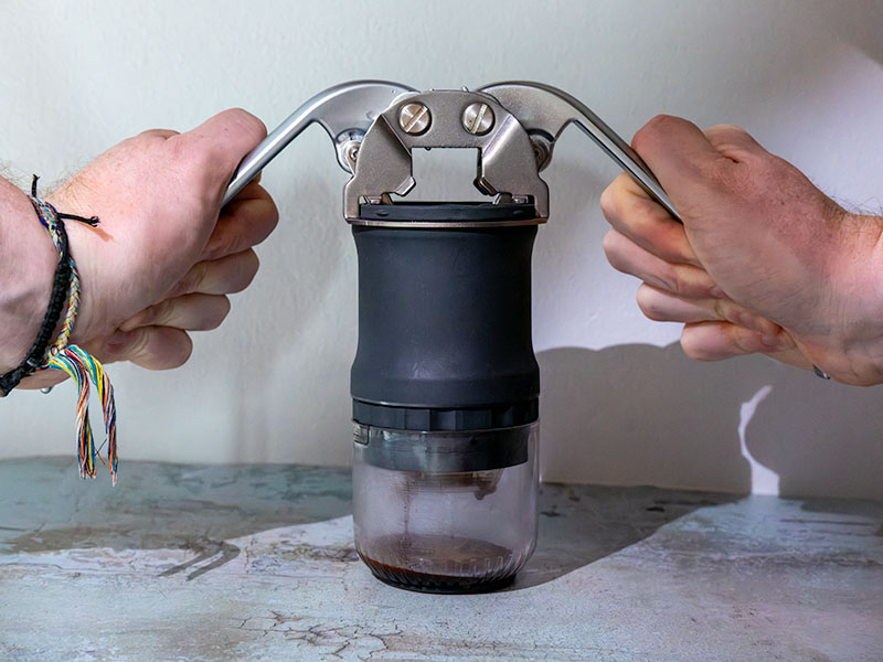 Hands pulling down the lever handles of the HUGH Leverpresso Lite V4, with an espresso shot starting to pour into the attached cup