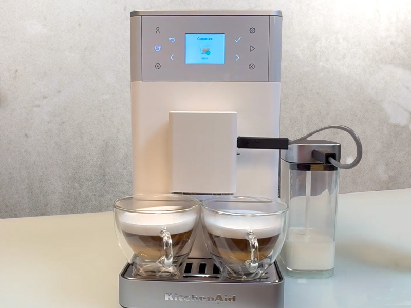 Two cappuccinos on the drip tray for the KitchenAid KF3 with milk carafe to the side