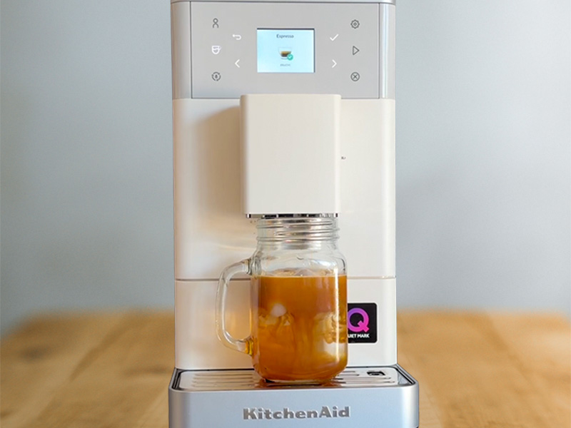 A freshly made iced espresso in a mason jar cup, sitting on the drip tray of KitchenAid KF3
