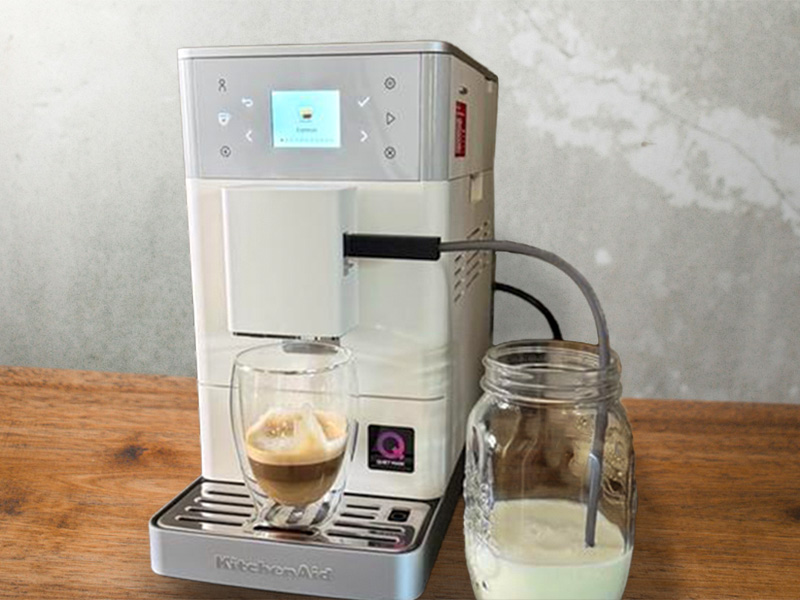 KitchenAid KF3 with a freshly made latte on the drip tray, milk hose going into a mason jar