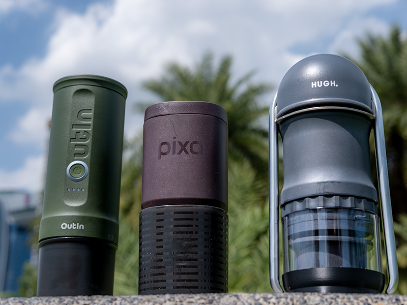 3 portable espresso machines - the OutIn Nano, Wacaco Pixapresso, and HUGH Leverpresso Lite V4 - sitting on a wall in the park