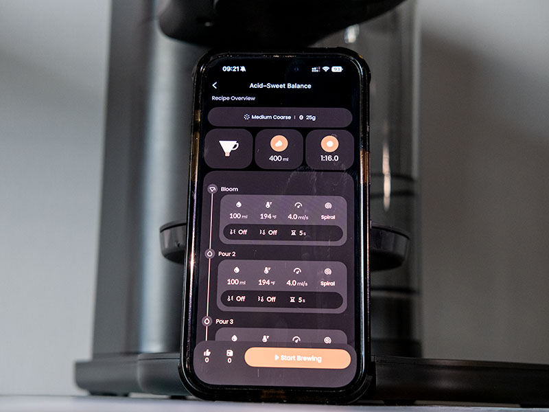 Mobile phone leaning on the Cosori Juni auto pour over coffee machine open on a recipe and brewing instructions with button to 'Start Brewing'