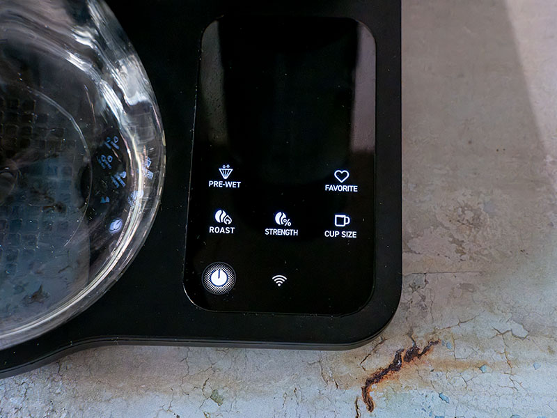Close-up of the small screen/user interface of the Cosori Juni with buttons for Pre-Wet, Favorite, Roast, Strength, Cup-size, On/Off, and Wifi